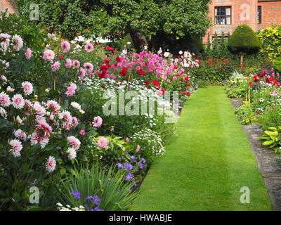 Chenies Manor sunken garden, Buckinghamshire nel sett. Dahlia display in piena fioritura, di fronte alla casa padronale con prato, fiori di frontiera, topiaria da, trellis. Foto Stock