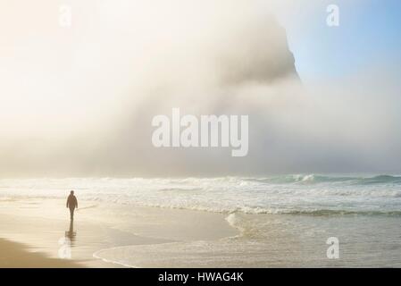 Norvegia, Nordland, isole Lofoten, isola Moskenesoy, donna camminando lungo la spiaggia isolata di Kvalvika, rottura sole attraverso la nebbia Foto Stock