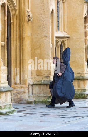 Cirencester - uomo che porta contrabbasso strumento musicale entrando in San Giovanni Battista a Cirencester, Gloucestershire in Marzo Foto Stock