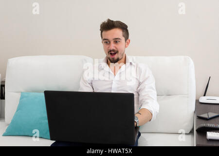 Sorpreso sconvolto l'uomo con la bocca aperta il lavoro a casa con il computer portatile Foto Stock