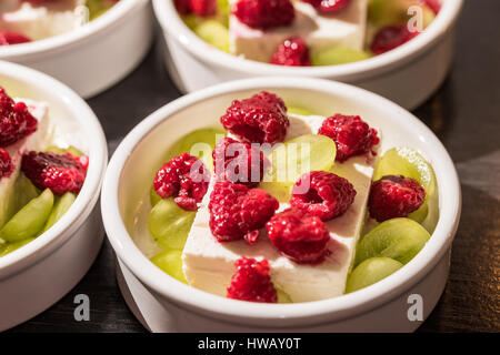 Bianco da dessert ciotole con Pigoli di formaggio, uva verde e rosso rasperries prima di grigliare in forno Foto Stock