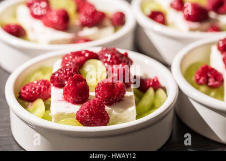 Bianco da dessert ciotole con Pigoli di formaggio, uva verde e rosso rasperries prima di grigliare in forno Foto Stock