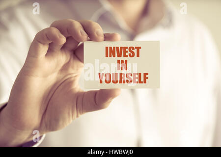 Primo piano su imprenditore tenendo una scheda con testo di INVESTIRE IN TE STESSO, business Concetto di immagine con soft focus background e tono vintage Foto Stock