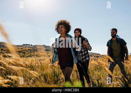 Gruppo di amici a piedi attraverso la campagna insieme. Felice di giovani uomini e donne escursionismo insieme su un giorno d'estate. Foto Stock