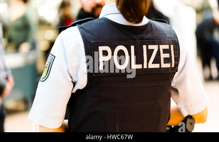 Il tedesco ufficiale di polizia donna sull'aeroporto di Amburgo osserva i passeggeri. Torna shot focus sul giubbotto antiproiettile con Polizei badget. Flughafen Hamburg, 13 Foto Stock