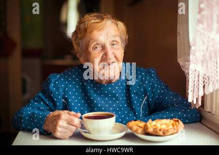 Donna anziana bere il tè seduto in cucina. Foto Stock