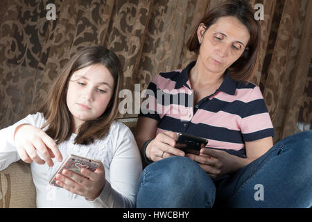 Madre e figlia in salotto sostenendo e tenere i telefoni cellulari Foto Stock