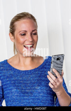 Una giovane donna è felice circa un SMS sul suo telefono cellulare ha concordato., Eine junge Frau freut sich "ber eine SMS die sie auf ihr Handy bekommen hat. Foto Stock