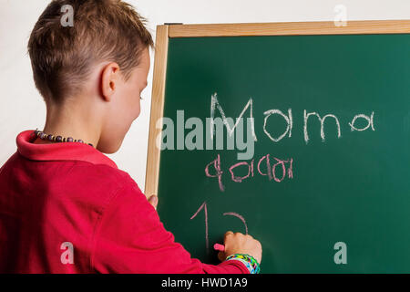 " Un Bambino scrive la parola "false" su un bordo della scuola", ein tipo schreibt das Wort ' Mama ' auf eine Schultafel Foto Stock