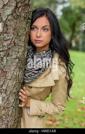 Una giovane donna vede dietro un albero in uscita, Eine junge Frau sieht hinter einem Baum hervor Foto Stock