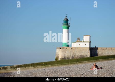 Francia, Seine Maritime, Le Treport, giovane seduto sulla spiaggia ghiaiosa di fronte il faro alla fine del molo Foto Stock