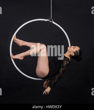 Antenna acrobat nell'anello. Una giovane donna esegue gli elementi acrobatici nell'anello dell'aria. Riprese in studio su sfondo nero. Foto Stock