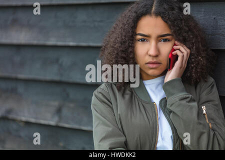 Outdoor ritratto della bella triste aggressiva di razza mista americano africano ragazza adolescente femmine giovane donna che parla su rosso telefono cellulare indossando bomba verde Foto Stock