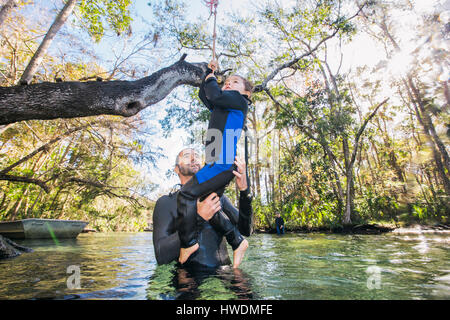 Padre nel fiume aiutando la figlia con swing corda su albero, Chassahowitzka, Florida, Stati Uniti d'America Foto Stock