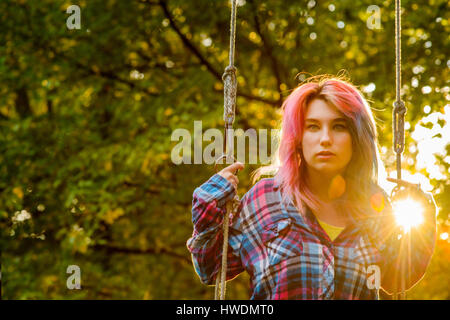 Ritratto di ragazza adolescente con multi-capelli colorati, su giardino swing Foto Stock