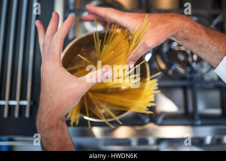 Chef di mettere gli spaghetti in pentola sulla stufa, close-up, vista aerea Foto Stock