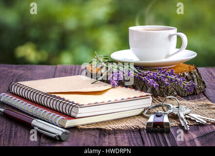 Vuoto notebook bianco,le chiavi, mazzetto di lavanda e tazza di caffè sulla scrivania all'aperto in estate Foto Stock