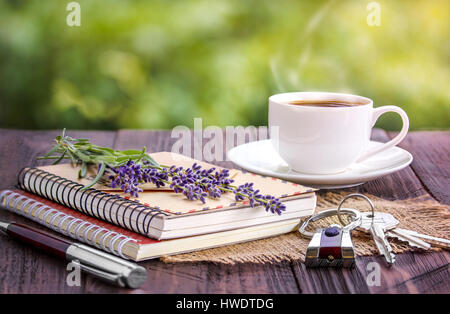 Vuoto notebook bianco,le chiavi, mazzetto di lavanda e tazza di caffè sulla scrivania all'aperto in estate Foto Stock