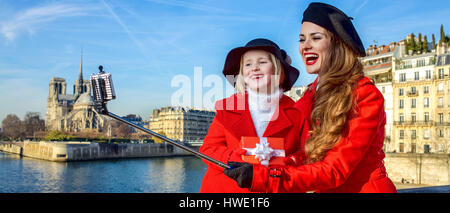 Luminose a Parigi. alla moda di madre e bambino i viaggiatori in rosso strati sul terrapieno a Parigi, in Francia con il regalo di Natale box prendendo selfie utilizzando selfie Foto Stock