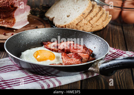 Fette di pancetta affumicata e uova fritte in padella. Abitudini alimentari concetto Foto Stock