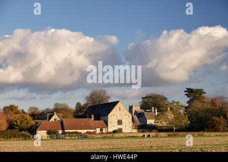 Vista su superfici agricole verso il villaggio di Somerford Keynes nel Gloucestershire con convertito fienili e torre di una chiesa Foto Stock