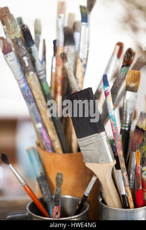 Set di pennelli per dipingere in una giara e mug sul tavolo di legno Foto Stock