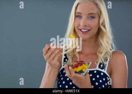 Ritratto di donna di mangiare insalata di frutta in vaso contro uno sfondo grigio Foto Stock