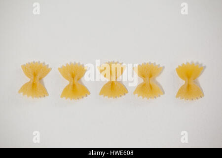 Farfalle di pasta disposte in una fila su sfondo bianco Foto Stock
