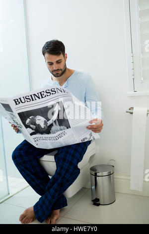 Uomo seduto sul sedile di gabinetto di lettura di un quotidiano a casa Foto Stock