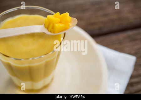 Vetro fresco di smoothie mantenuta sulla piastra con ananas in cucchiaio sul tavolo di legno Foto Stock