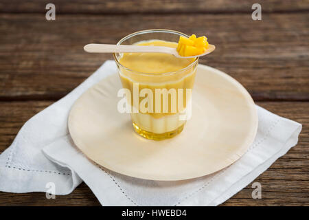 Vetro fresco di smoothie mantenuta sulla piastra con ananas in cucchiaio sul tavolo di legno Foto Stock