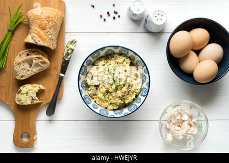 In casa insalata di uova diffondersi con maionese, mostarda, cipolla rossa cosparso con erba cipollina, vista dall'alto su sfondo bianco da tavola. Foto Stock