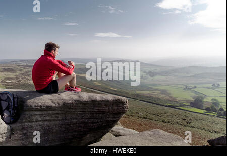 Runner maschile seduto a guardare fuori dalla parte superiore del bordo Stanage, Peak District, Derbyshire, Regno Unito Foto Stock