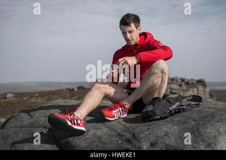 Runner maschio spuntini di apertura sulla parte superiore del bordo Stanage, Peak District, Derbyshire, Regno Unito Foto Stock