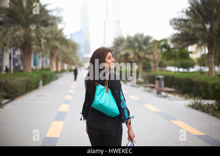 Vista posteriore della femmina matura shopper il trasporto delle borse della spesa, Dubai, Emirati Arabi Uniti Foto Stock