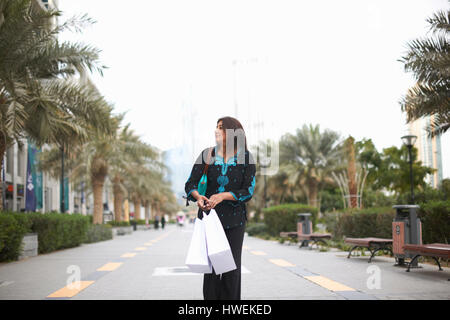 Femmina matura shopper passeggiando con le borse della spesa, Dubai, Emirati Arabi Uniti Foto Stock