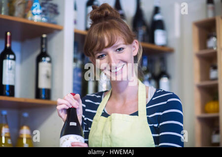 Ritratto di giovane donna in negozio, tenendo in mano una bottiglia di vino Foto Stock