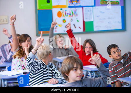 Gli studenti in aula, seduto alla scrivania, con le braccia sollevate Foto Stock