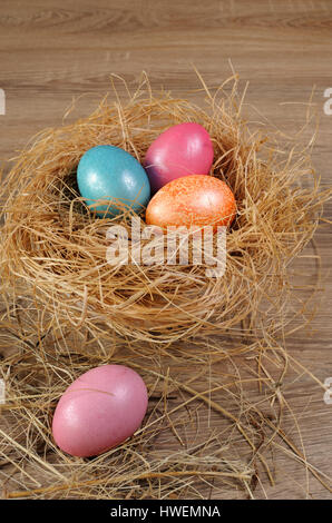 Decorazioni per la Pasqua. Colorate le uova di pollo in un nido di fieno su uno sfondo di legno Foto Stock