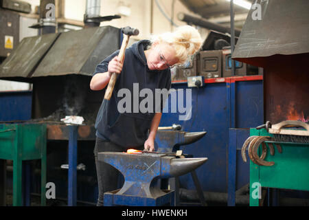 Femmina giovane apprendista fabbro ferro di cavallo di martellamento sui workshop incudine Foto Stock