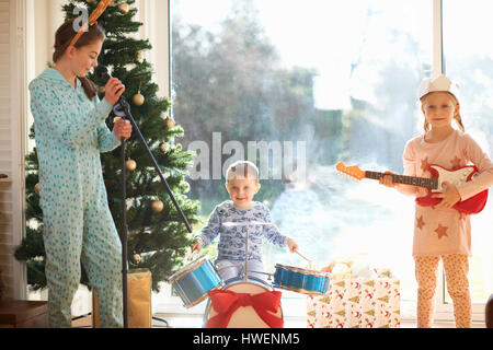 Ragazzo e sorelle giocando toy drum kit e chitarra il giorno di Natale Foto Stock