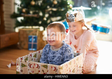 Ragazza spingendo il fratello in una scatola di cartone a natale Foto Stock