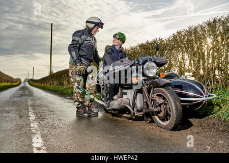 Maschio Senior motociclista a parlare con il nipote seduto sul motociclo su strada rurale Foto Stock