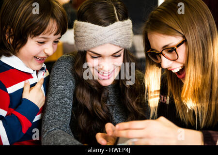 Due giovani donne e ragazzo cerca e ridere per smartphone nel cafe Foto Stock