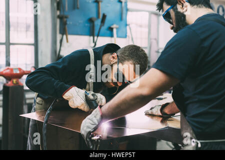 Team di lamiera di rame di taglio con la torcia di saldatura in forge workshop Foto Stock