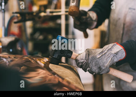 Mani di metallurgo martellare il rame in forge workshop Foto Stock