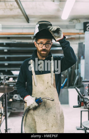 Ritratto di metallurgo tenendo la torcia di saldatura in forge workshop Foto Stock