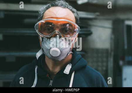 Ritratto di metallurgo nella maschera di protezione contro la polvere e gli occhiali di protezione in forge workshop Foto Stock