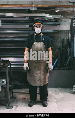 Ritratto di lavoratore metalmeccanico maschio in maschera antipolvere, forge ripostiglio Foto Stock