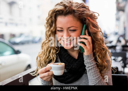 Donna in cafe azienda tazzina rendendo chiamata telefonica sorridente Foto Stock